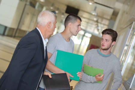 male teacher walking in corridor with studentsの写真素材