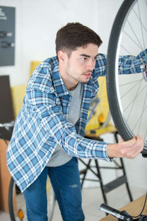 mechanic serviceman adjusting bicycle gear on wheel in workshopの写真素材