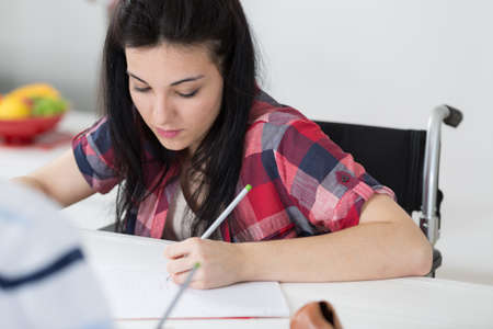 invalid girl writing in a notepad on wheelchairの写真素材