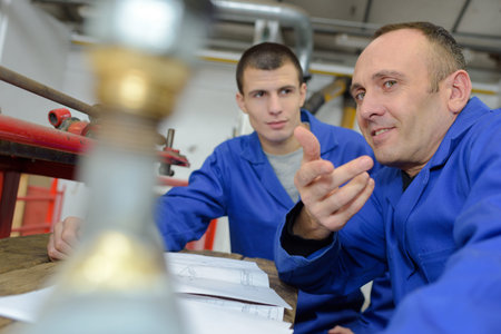 young technician working on machine in workshop with co-worker