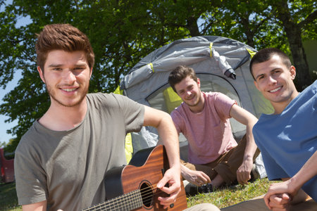 Three young men sat around tentの写真素材
