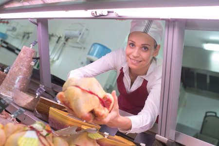 portrait of female butcher offering raw meatの写真素材