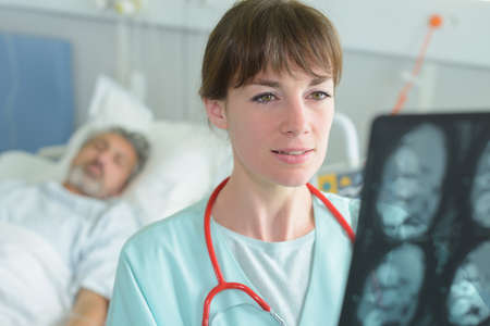 Doctor looking at xray, patient in hospital bed in backgroundの写真素材