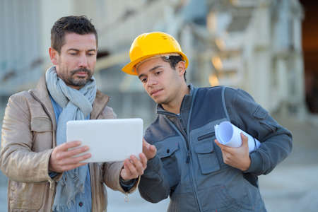 constructor and manager working on modern tablet outside renovated factoryの写真素材