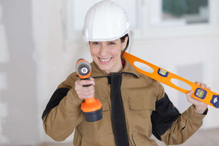 happy female worker with tool level and drill at workの写真素材
