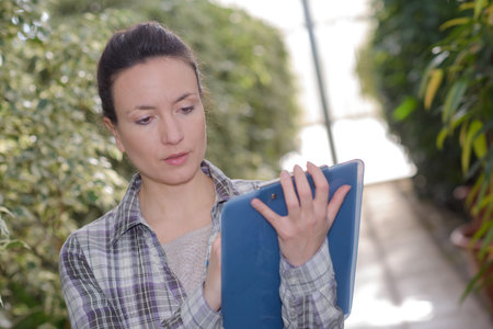gardener with clipboard in garden center checking growth of plants
