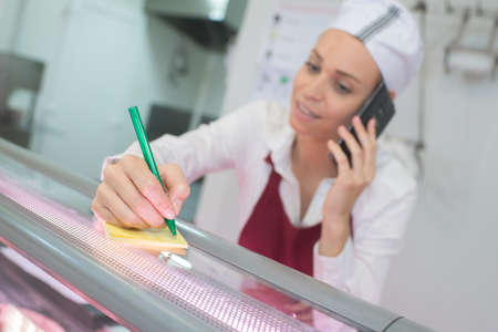 female butcher on the phone behind counterの写真素材