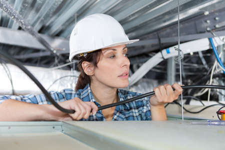 female worker checking wires and cables on the ceilingの写真素材