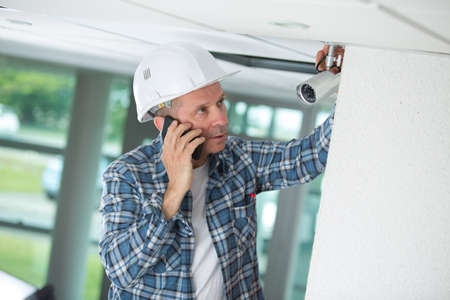 worried male technician installing camera on wallの写真素材