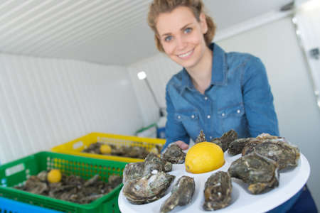 woman showing oysters on a metal tray with lemonの写真素材