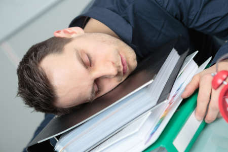Man asleep on stack of foldersの写真素材