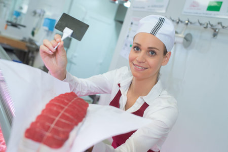 Female butcher holding joint of beef and blank labelの写真素材
