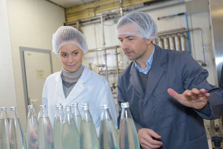 People in factory looking at glass bottlesの写真素材