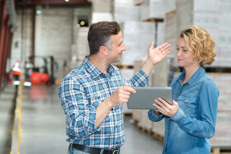 warehouse manager and worker looking at tablet in warehouseの写真素材