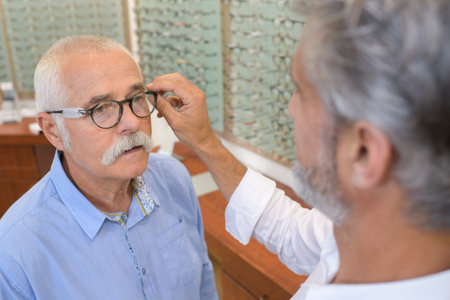 senior man trying spectacles frames at opticianの写真素材