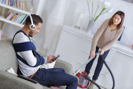 woman cleaning up while husband is relaxing on the sofaの写真素材