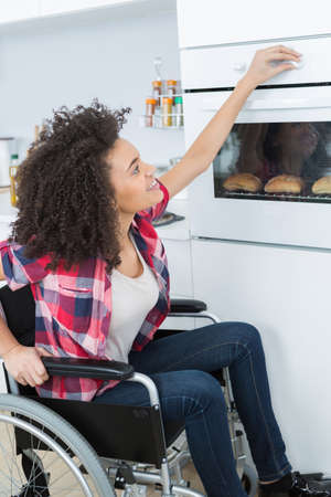 disabled young woman in wheelchair opens the ovenの写真素材