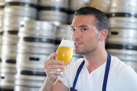 handsome young male brewer in apron tasting fresh beerの写真素材