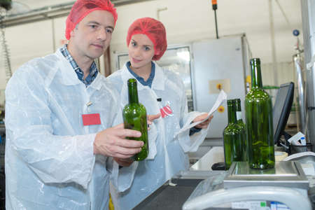 co-workers examining bottles at bottling plantの写真素材