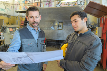 architect and manual worker examining blueprint at table in industry