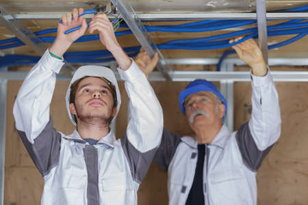 young male electrician with mentor wiring in ceilingの写真素材