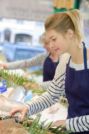 young saleswoman offers fresh fish in a shopの写真素材