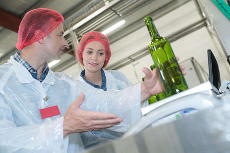 cheerful man and woman wearing uniform standing in bottling factoryの写真素材