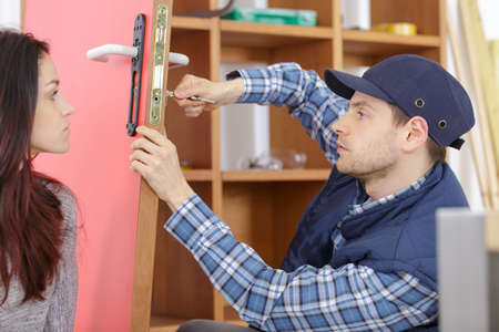 cheerful locksmith installing a door lock under clients surveillanceの写真素材