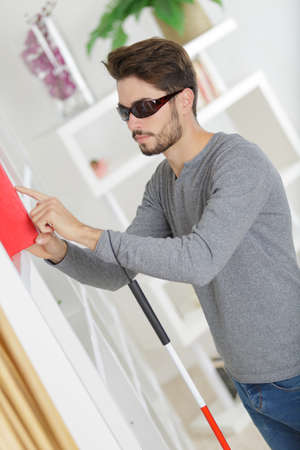 blind young man with stick and dark glasses at homeの写真素材