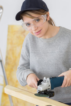 female carpenter using electric sander for wood