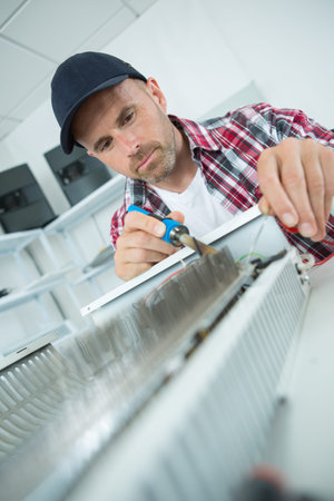male plumber repairing radiator with a soldering iron