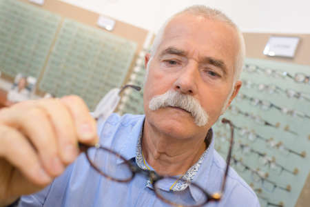 senior male customer choosing glasses in optics storeの写真素材