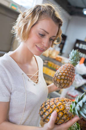 woman choosing fruits at supermarket and holding pineappleの写真素材