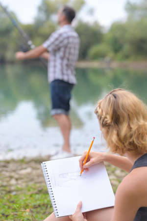 woman drawing while boyfriend fishesの写真素材