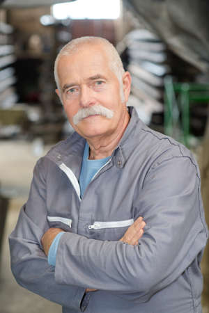 confident senior worker standing with arms crossed in workshopの写真素材