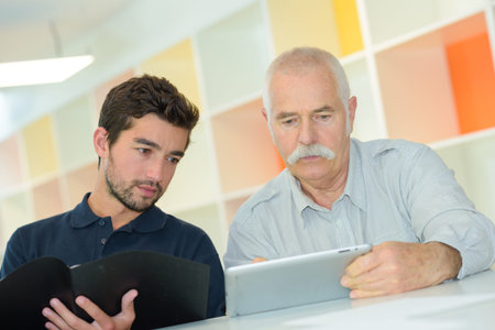 grandson is teaching his grandfather to use digital tabletの写真素材
