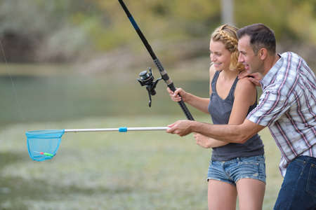lovely young couple fishing together by a lakeの写真素材