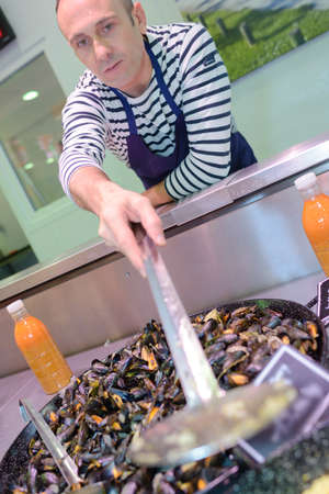 Happy seller in apron showing musselsの写真素材