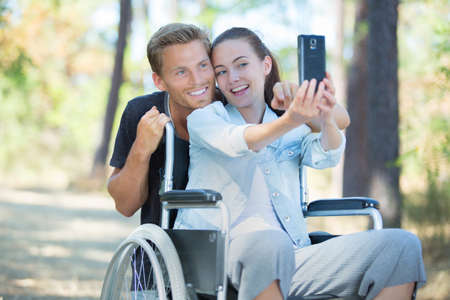 woman in wheelchair and boyfriend taking a selfie with smartphoneの写真素材