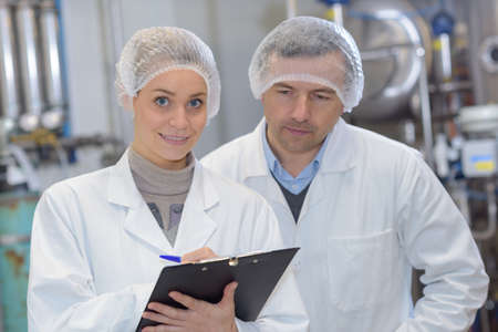Man and woman wearing hair nets making notes on clipboardの写真素材