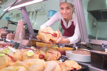 Female butcher holding raw chickenの写真素材