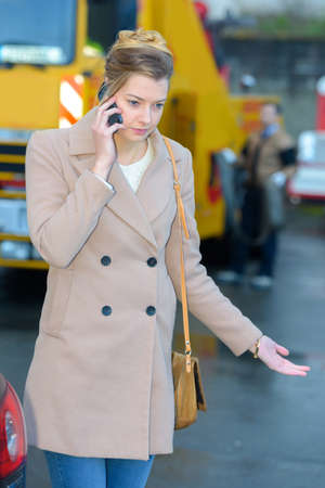 Frustrated lady on telephone, breakdown truck in backgroundの写真素材