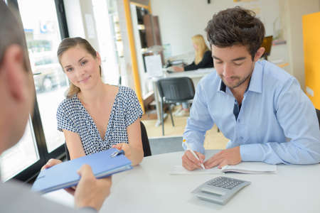 Couple in office receiving file from agentの写真素材