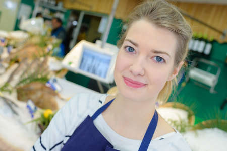 portrait of positive female shop assistant selling fresh fishの写真素材