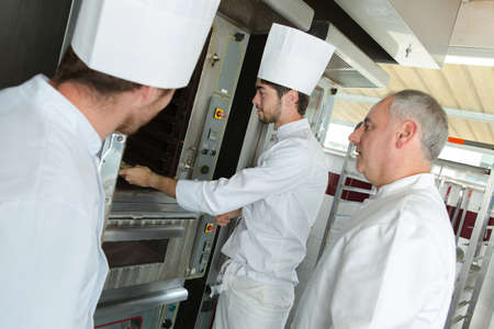 male baker and his assistants using the ovenの写真素材