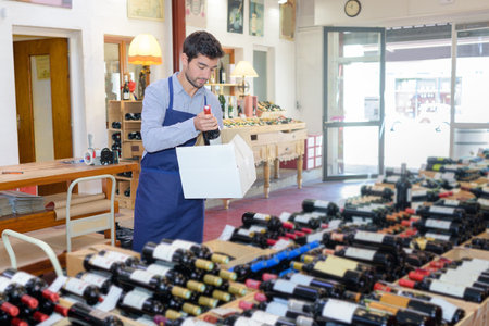 smiling seller man wearing apron promoting wine in wine storeの写真素材