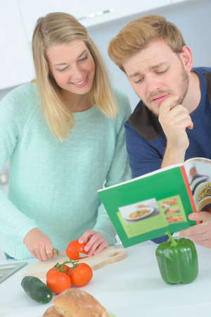 Couple looking at recipe book while chopping vegetablesの写真素材