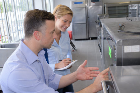 Man showing industrial kitchen equipment to woman with notebook