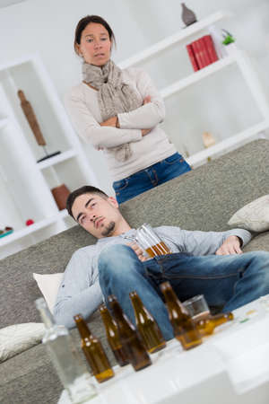 Woman looking disdainfully at young man surrounded by empty beer bottlesの写真素材