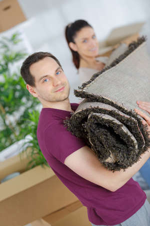 couple carrying a carpet at home in their new locationの写真素材